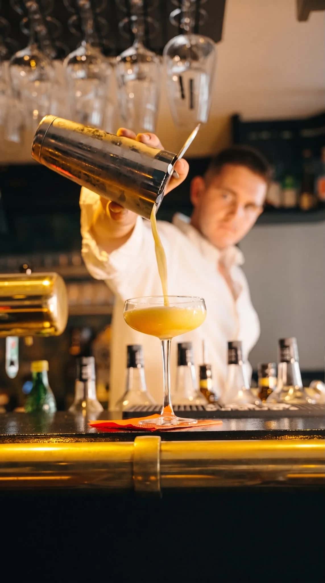 Hinter dem Tresen des FILOU wird ein Cocktail aus dem Shaker in ein Glas gegossen
